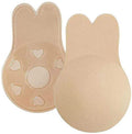 Shapelux Lifting Pads für unsichtbare Bruststraffung sind beigefarbene, wiederverwendbare Silikonüberzüge in Hasenohrform mit starkem Klebeband. Einer zeigt die glatte Vorderseite, der andere hat herzförmige Ausschnitte und strukturiertes Klebeband als Alternative zu einem trägerlosen BH.