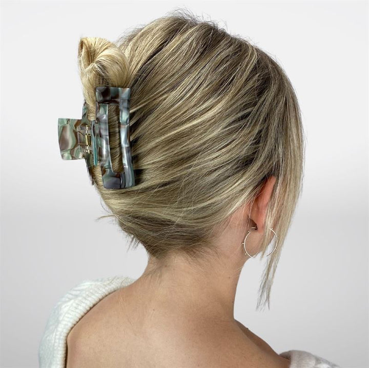 A person with blonde hair in a French twist, secured by the SOHO Aria Hair Claw in Pearl Green, wears a white top and hoop earrings, photographed from behind against a white background.
