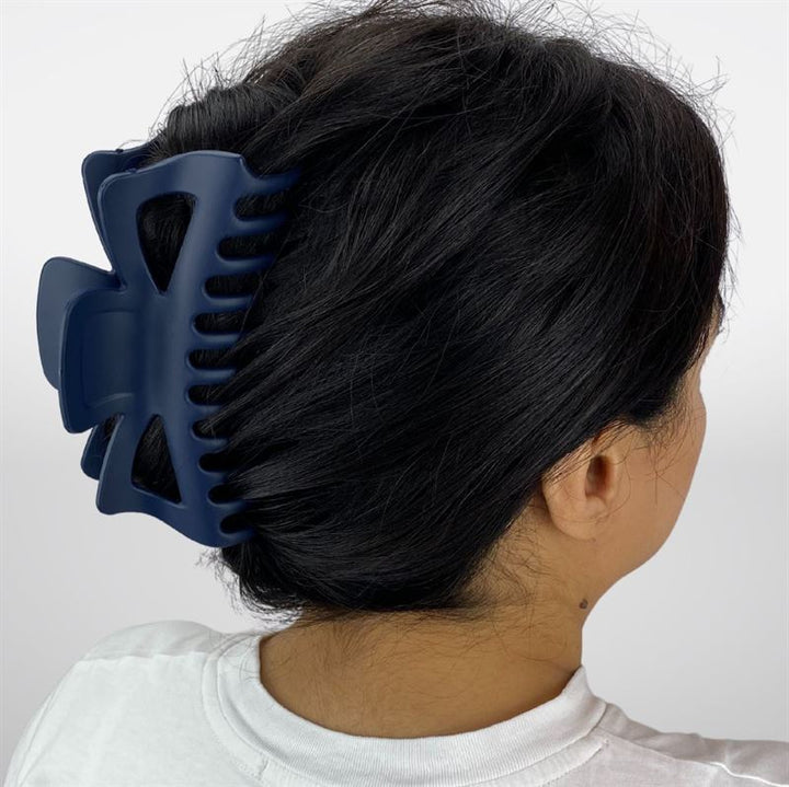 A woman with dark hair in a twist, secured by the SOHO Astrid Hair Claw - Navy from SOHO, is shown from behind wearing a white shirt.
