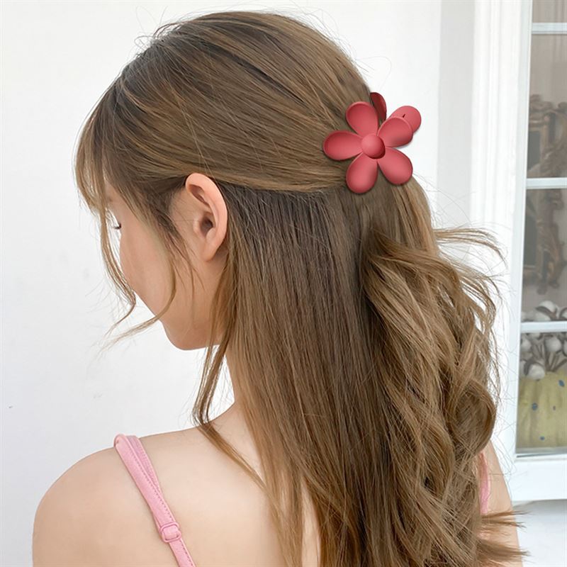 A woman with long, wavy brown hair styles her hair using the SOHO Bloom Hair Claw - Brown by SOHO. She wears a pink strappy top and stands against a white background.