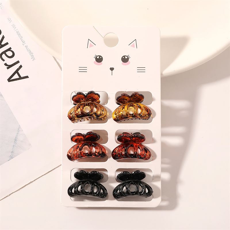 The SOHO Fika Mini Hair Claws set by SOHO includes six small claws in brown, orange, and black, displayed on a cute cat face card and shown on a white surface near a plate and paper.