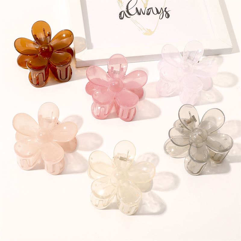The SOHO Fiore Hair Claw - Charm Pink by SOHO is displayed on a white surface among other colorful clips, with framed "always" artwork in the background.