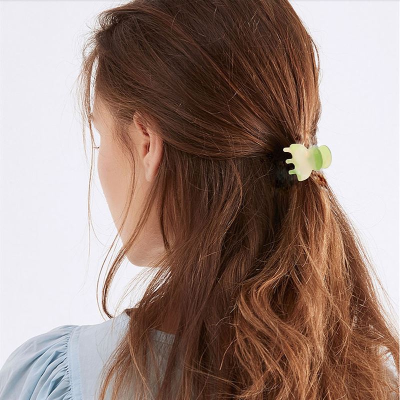 A woman with long brown hair, seen from behind in a light blue top, secures her half-up hairstyle with the SOHO Hara Mini Hair Claw in Clay by SOHO.