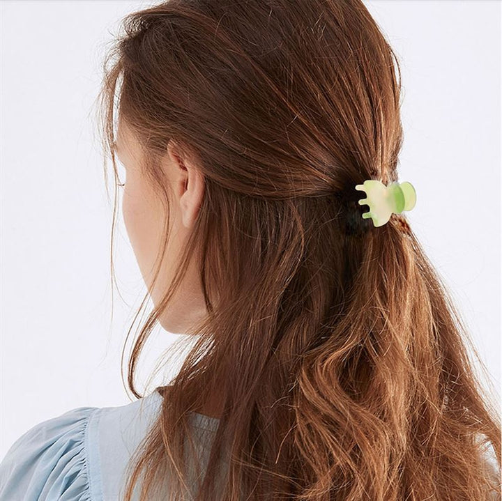 A woman with long brown hair, seen from behind, wears a pale blue top and secures her half-up hairstyle with the SOHO Hara Mini Hair Claw in Porcelain by SOHO.