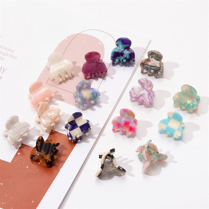 SOHO Hara Mini Hair Claw - Porcelain clips by SOHO, featuring marbled, checkered, and solid styles in assorted colors and shapes, are arranged on a white surface and magazine page for a secure hair grip.