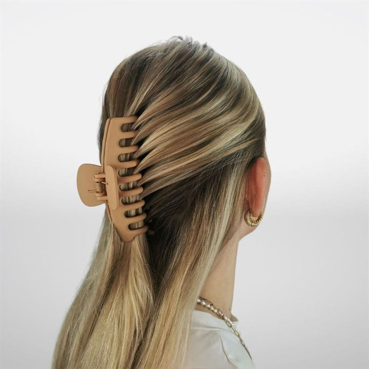 A woman with blonde hair, styled half-up using the SOHO Kana Hair Claw - Sepia by SOHO, is shown from behind. She wears gold hoop earrings and a pearl necklace against a plain light background.