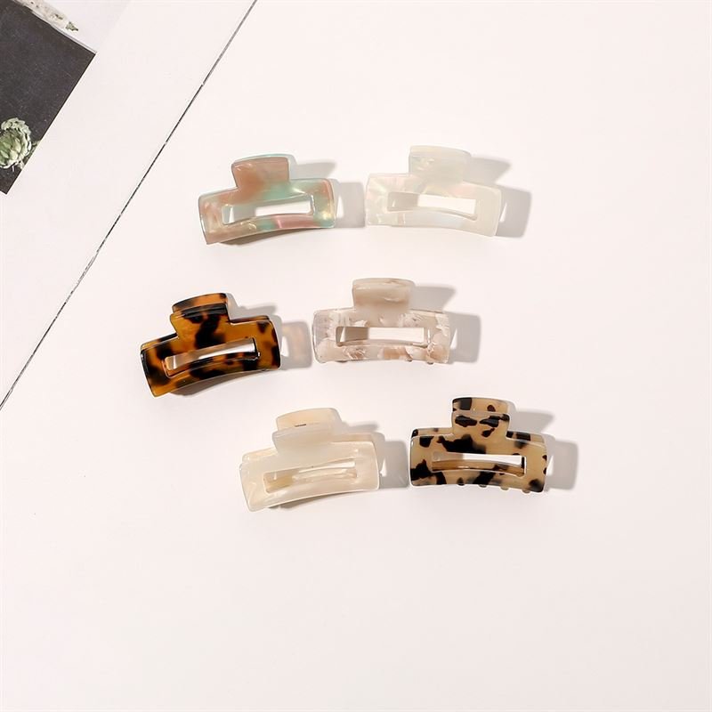Six SOHO Leia Mini Hair Claws in assorted colors and patterns, including tortoiseshell, cream, and marbled designs, are neatly arranged on a light surface with a magazine in view—perfect for stylish hairstyling.