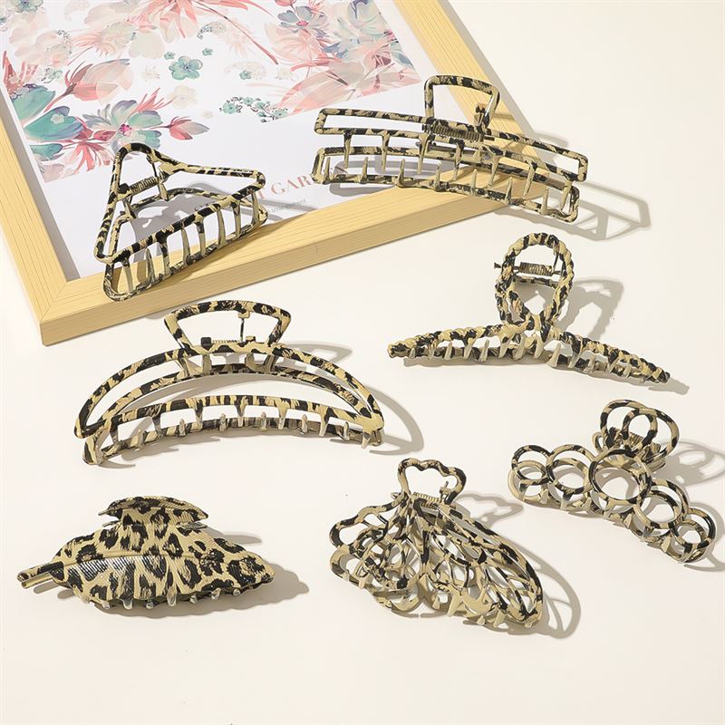 Seven SOHO Leopard Metal Barette Hair Claws by SOHO, styled in beige, black, and brown leopard patterns, are displayed on a cream surface beside a floral-framed picture.