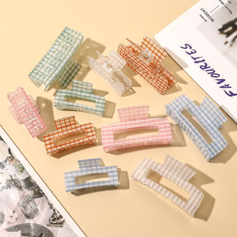 The SOHO Line Hair Claw - Green by SOHO features a colorful plaid design and offers a secure hold, making it a stylish hair accessory for any look. Pictured on a beige surface beside a magazine and floral-patterned fabric.