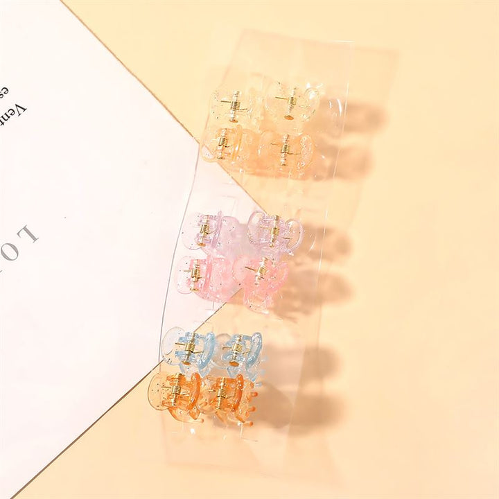 The SOHO Lucca Mini Hair Claws - Glitter by SOHO feature pastel yellow, pink, and blue designs on a clear strip, adding a charming touch to your style. Displayed on beige next to a white paper for a stylish presentation.