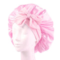 Die SOHO Makena Satin Bonnet – Pink von Fashiongirl, die auf einem Mannequin-Kopf präsentiert wird, verfügt über ein glänzendes rosa Satin-Finish und eine große Schleife auf der Vorderseite – ideal zum Schutz der Haare und zur Vermeidung von Frizz.