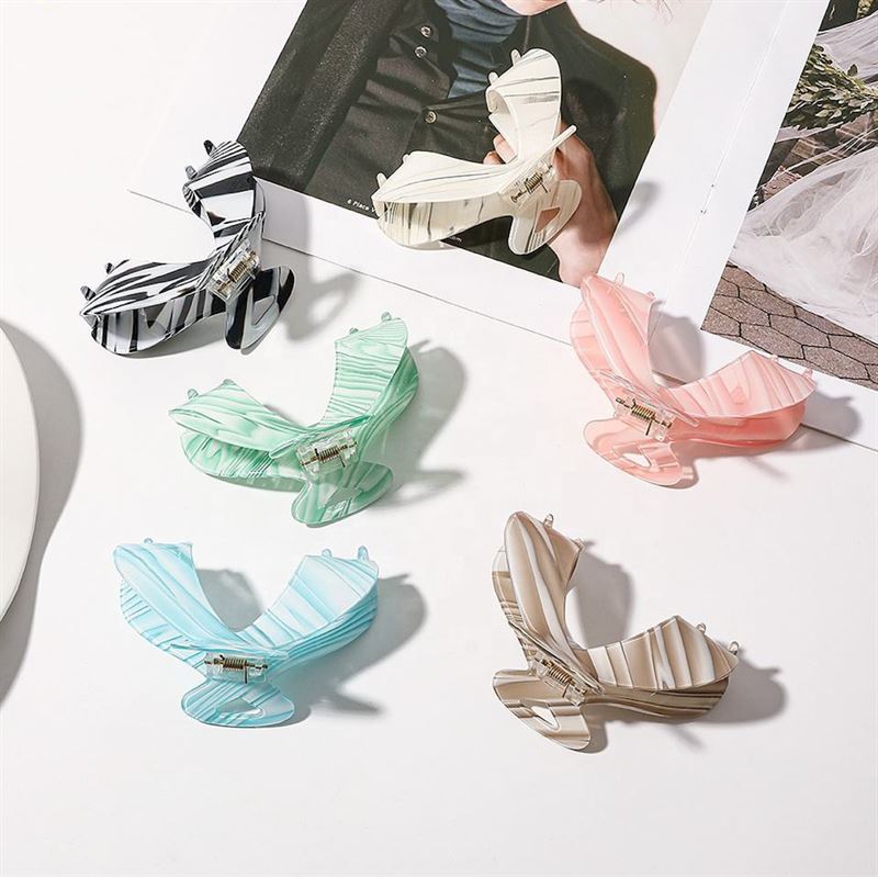 The SOHO Malou Hair Claw - Green by SOHO is displayed on a white surface beside an open fashion magazine, featuring a butterfly shape and stylish pastel and striped design.