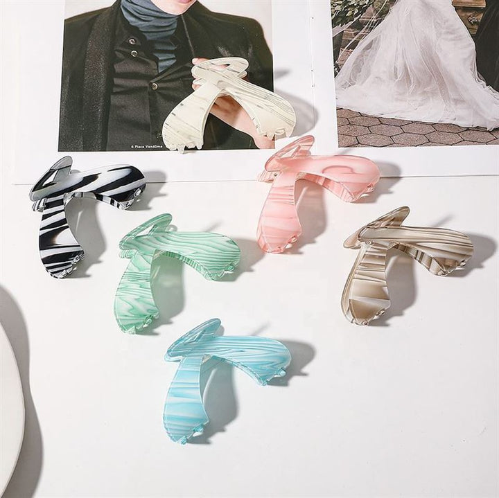 The SOHO Malou Hair Claw - Green by SOHO is displayed on a white surface beside magazines. This stylish claw comes in a vibrant green shade, part of a colorful collection that includes pastel and classic tones.