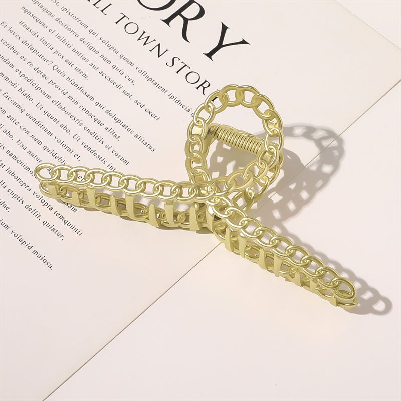 The SOHO Monz Metal Hair Claw in gold by SOHO sits atop an open book, casting a delicate shadow over English and foreign text—a sophisticated hair accessory that elevates your reading experience.