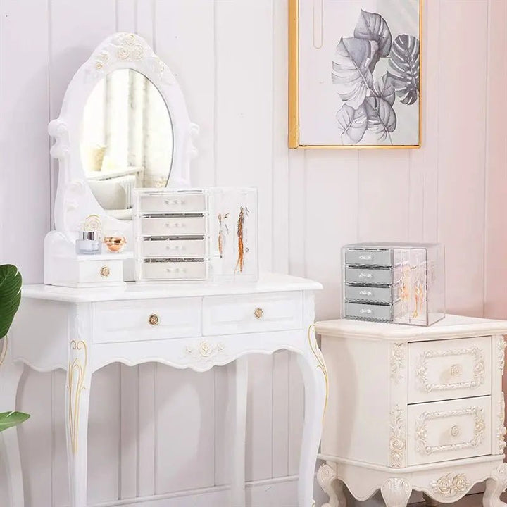 A UNIQ Acrylic Jewellery Organiser with 4 drawers and 2 earring holders (SF 1142) sits beside a matching nightstand in a softly lit room, while a framed leaf artwork hangs on the pale-paneled wall.